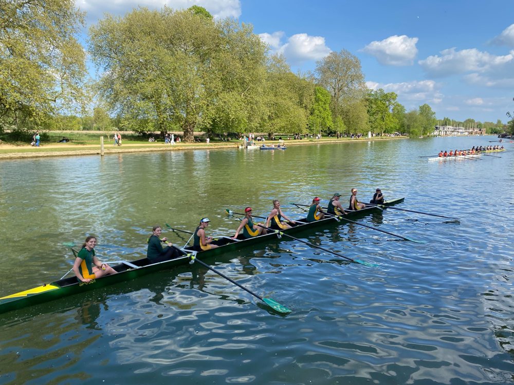A women's eight smiling on the Isis on a sunny day